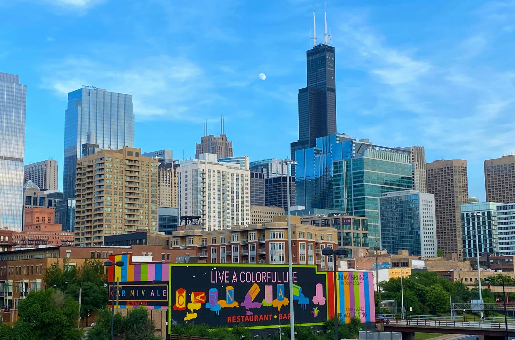 A colorful billboard-scale mural in front of the Chicago skyline and the Willis Tower